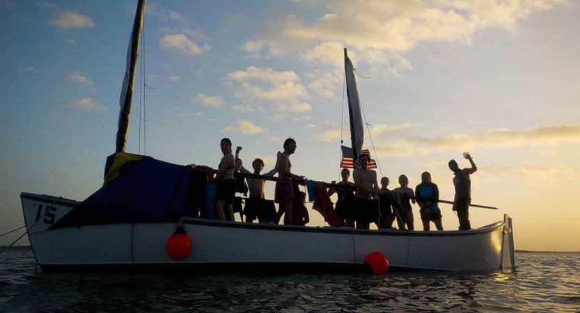 the silhouette of a group of people on a sailboat at sunset